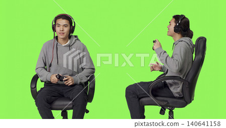 Skilled man playing online videogames in studio, having fun with people on gaming multiplayer challenge over green screen backdrop, Asian guy enjoying competition with gamers. Skilled man playing online videogames in studio, having fun with people on gaming multiplayer challenge over green screen backdrop, Asian guy enjoying competition with gamers. 140641158