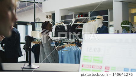 Pregnant woman looking at trendy merchandise on stand hangers, shopping for pregnancy clothes in fashion store at mall. Pregnant woman looking at trendy merchandise on stand hangers, shopping for pregnancy clothes in fashion store at mall. 140641276