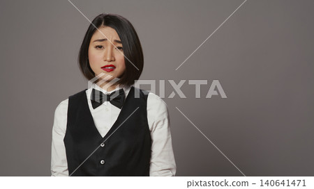 Bored receptionist being confused and overworked in studio, posing with confusion and fatigue over grey background, Asian administrator feeling uncertain and unsure about something. 140641471