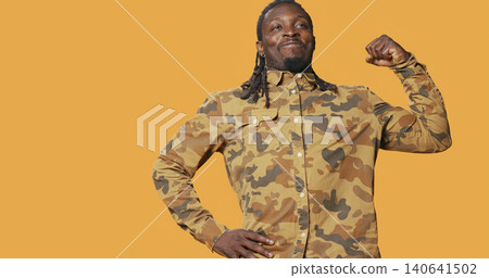 Athletic strong man flexing his biceps muscles on camera, advertising fitness routine and wellbeing. Athletic strong man flexing his biceps muscles on camera, advertising fitness routine and wellbeing. 140641502