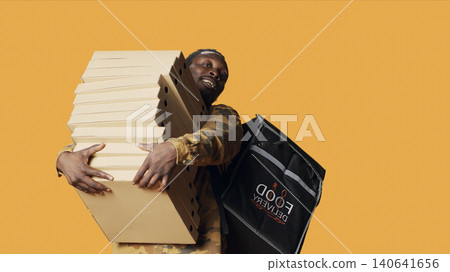 Young deliveryman giving huge stack of pizza boxes to client, delivering big fast food order and carrying takeaway backpack, with male model posing as delivery person with takeout food. Young deliveryman giving huge stack of pizza boxes to client, delivering big fast food order and carrying takeaway backpack, with male model posing as delivery person with takeout food. 140641656