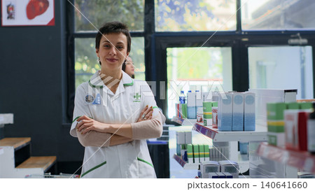 Friendly pharmacist in pharmacy waiting for customers to arrive, placing pharmaceutical products on shelves, with smiling healthcare specialist in drugstore showing confidence and expertise. Friendly pharmacist in pharmacy waiting for customers to arrive, placing pharmaceutical products on shelves, with smiling healthcare specialist in drugstore showing confidence and expertise. 140641660