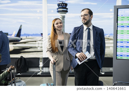 Two professionals, airport terminal, business trip, in waiting area at the gate, walking with luggage and checking boarding passes. Global business teamwork and preparation for international flight. 140641661