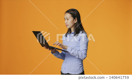 Casual person navigating online on laptop in studio, looking for inspiration on wireless computer against orange background. 140641759
