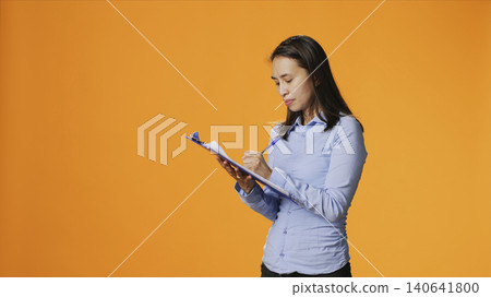Filipino model writes information on files with clipboard, taking notes to create full report in front of camera, with young adult in casual clothing filling in documents, keeping track of something. Filipino model writes information on files with clipboard, taking notes to create full report in front of camera, with young adult in casual clothing filling in documents, keeping track of something. 140641800