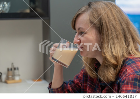Woman thoughtfully assesses plant based milk in compact kitchen setting, Female expert skillfully tests and analyzes plant derived milk in modest kitchen environment for flavor and consistency 140641817