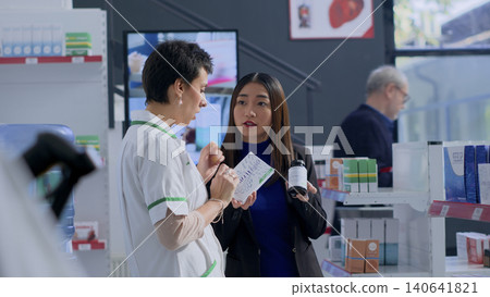 Experienced healthcare professional in pharmacy helping customer with medical suggestions, with client wishing to purchase supplements and vitamins, asking pharmacist for recommendations. Experienced healthcare professional in pharmacy helping customer with medical suggestions, with client wishing to purchase supplements and vitamins, asking pharmacist for recommendations. 140641821