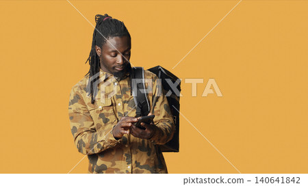 Male courier delivering fast food restaurant order with backpack, bringing takeaway meal for client at their home, with deliveryman working on takeout with thermal bag, looking for the address. Male courier delivering fast food restaurant order with backpack, bringing takeaway meal for client at their home, with deliveryman working on takeout with thermal bag, looking for the address. 140641842