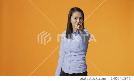 Model pointing at the camera in colorful studio, looking into the lens with confidence, with young filipino woman points index finger and standing proud against orange background. Model pointing at the camera in colorful studio, looking into the lens with confidence, with young filipino woman points index finger and standing proud against orange background. 140641845