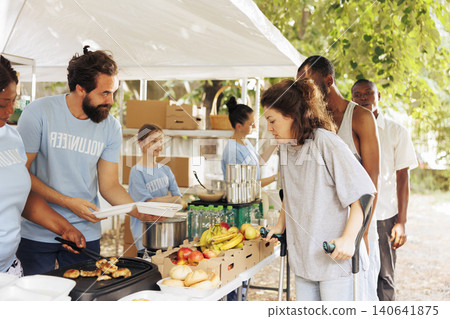Multiethnic group of volunteers providing humanitarian aid to disadvantaged individuals, with caring charity workers distribute free food and donations, helping the homeless, sick, and needy people. 140641875