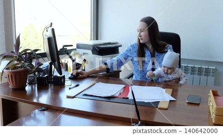 Professional woman multitasking with baby in office environment, using computer mouse and managing work and motherhood 140642000