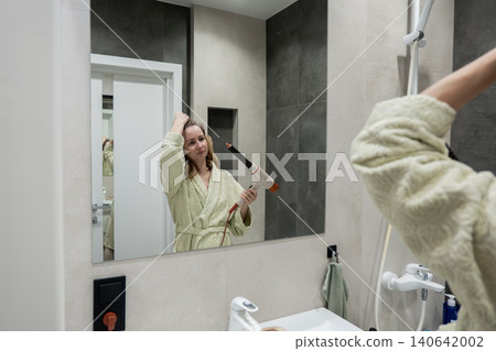 Caucasian woman at mirror brushing hair in bathrobe, concentrated expression, practicing poses and styling techniques, modern sink and vanity visible, prepping for studio photoshoot with poised Caucasian woman at mirror brushing hair in bathrobe, concentrated expression, practicing poses and styling techniques, modern sink and vanity visible, prepping for studio photoshoot with poised 140642002