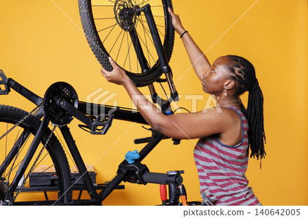 Meticulous woman repairs broken bike, adjusting the gears and securing the wheel with expert precision, with sporty woman examining and changing tire of bicycle. 140642005