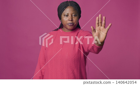 Woman with denying using stop hand gesture towards camera against isolated background, with female fashion influencer disapproving rejecting disagree portrait on pink background. Woman with denying using stop hand gesture towards camera against isolated background, with female fashion influencer disapproving rejecting disagree portrait on pink background. 140642054