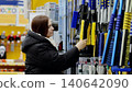 Woman selecting a snow brush for her car at a supermarket, reaching for the yellow brush on a shelf with various brushes and cleaning supplies 140642090