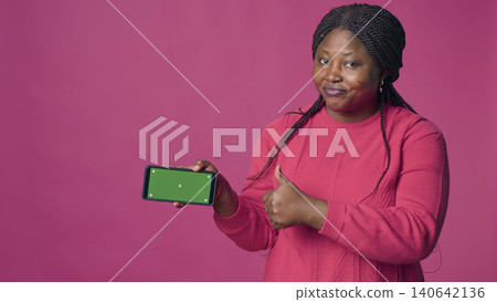 Enthusiastic woman horizontally grasping cell phone with blank chroma key template, with positive woman carrying mobile phone showing isolated green screen display. Enthusiastic woman horizontally grasping cell phone with blank chroma key template, with positive woman carrying mobile phone showing isolated green screen display. 140642136