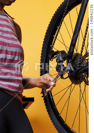 Close up shot of a woman hand holding specialized spanner for securing and adjusting bike hub and axle, with detailed image showing a wrench being used for bicycle wheel maintenance. Close up shot of a woman hand holding specialized spanner for securing and adjusting bike hub and axle, with detailed image showing a wrench being used for bicycle wheel maintenance. 140642236