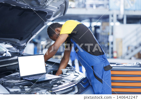 Mockup laptop on car with hood open while repairman in blurry background replaces motor, with isolated screen device next to adept garage professional fixing customer automobile. Mockup laptop on car with hood open while repairman in blurry background replaces motor, with isolated screen device next to adept garage professional fixing customer automobile. 140642247
