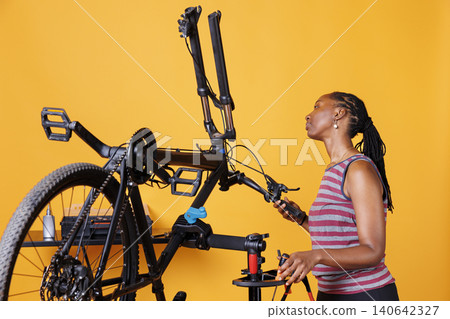 Female meticulously examining bike components and fixing front fork with specialized tools, with young woman inspects and maintains modern bicycle with care. Female meticulously examining bike components and fixing front fork with specialized tools, with young woman inspects and maintains modern bicycle with care. 140642327