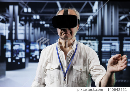 Senior developer immersed in virtual reality at data center, doing hardware maintenance, with professional using VR headset to optimize server rows system performance, harnessing advanced technology. 140642331