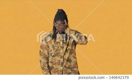 Man shows three wise monkeys sign standing over orange background, presenting symbol to not see, hear or speak. Man shows three wise monkeys sign standing over orange background, presenting symbol to not see, hear or speak. 140642370
