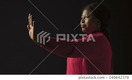 Woman firmly signals stop using hand gesture in isolated black background, with female fashion model expresses disapproval rejecting and disagreeing in side-view portrait shot. Woman firmly signals stop using hand gesture in isolated black background, with female fashion model expresses disapproval rejecting and disagreeing in side-view portrait shot. 140642378