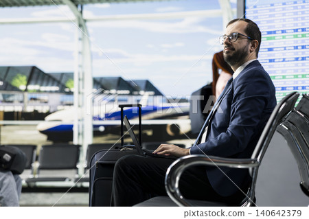 Corporate travel with consultant in a busy airport waiting area, checking flight details on laptop near the boarding gate. Professional prepares for departure, international business trip. Corporate travel with consultant in a busy airport waiting area, checking flight details on laptop near the boarding gate. Professional prepares for departure, international business trip. 140642379