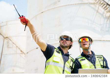 Two industrial engineers using laptop and walkie talkie at refinery Two industrial engineers using laptop and walkie talkie at refinery 140642384