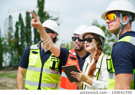 Diverse factory workers in safety vests discussing data outdoor Diverse factory workers in safety vests discussing data outdoor 140642399