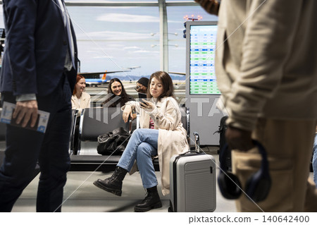 Smiling woman in airport texting friends while travelling to foreign country. Happy tourist in departure terminal chatting using mobile phone, waiting to catch plane for city break Smiling woman in airport texting friends while travelling to foreign country. Happy tourist in departure terminal chatting using mobile phone, waiting to catch plane for city break 140642400
