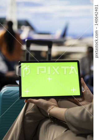 Green screen on tablet near crowd of tourists at airport boarding gate, ready for plane departure with luggage and backpacks. Passengers check schedule updates and airline information in terminal. Green screen on tablet near crowd of tourists at airport boarding gate, ready for plane departure with luggage and backpacks. Passengers check schedule updates and airline information in terminal. 140642401