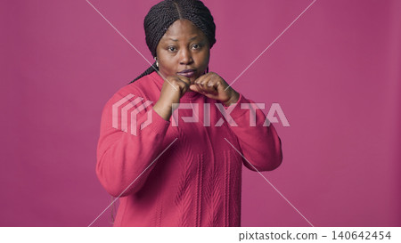 Confident woman with her hands clasped together showing ready for fighting, with woman with self-confidence posing with clenched fists against pink color background. Confident woman with her hands clasped together showing ready for fighting, with woman with self-confidence posing with clenched fists against pink color background. 140642454