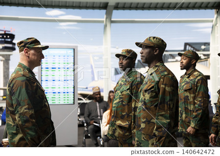 Military troops team receiving orders from veteran in airport terminal, standing in formation. Multiracial army squad wearing camouflage uniforms standing at attention in airport hub Military troops team receiving orders from veteran in airport terminal, standing in formation. Multiracial army squad wearing camouflage uniforms standing at attention in airport hub 140642472