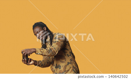 Cheerful adult playing rpg videogames on mobile gadget, having fun with gaming competition on smartphone in studio, with man enjoying shooting game with people, orange background. Cheerful adult playing rpg videogames on mobile gadget, having fun with gaming competition on smartphone in studio, with man enjoying shooting game with people, orange background. 140642502