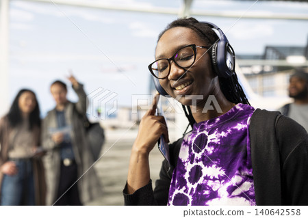 Carefree woman in airport enjoying music with audio device while waiting for plane. Happy girl wearing headphones listening to favorite songs in airport terminal Carefree woman in airport enjoying music with audio device while waiting for plane. Happy girl wearing headphones listening to favorite songs in airport terminal 140642558
