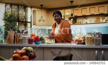 African american, influencer doing meal prep, salad bowl, cutting radish, and other vegetables on the cutting board. Vlogger woman filming a video with the cooking process and culinary advice. 140642701