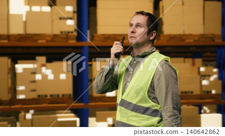 Warehouse operator reporting parcel status via two-way portable transceiver, ensuring teamwork through radio signal walkie-talkie in depot. Professional communication ensures order fulfillment. 140642862