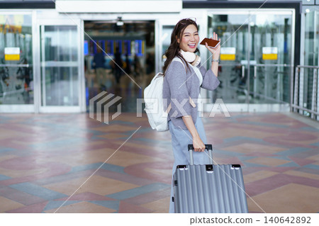 Female traveler standing at airport terminal with holding smartphone and passport Female traveler standing at airport terminal with holding smartphone and passport 140642892