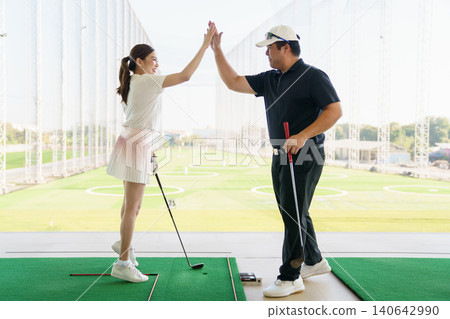 Woman learning golf swing technique with a coach at a driving range. Woman learning golf swing technique with a coach at a driving range. 140642990