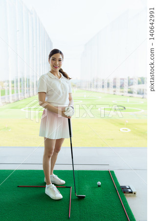 Woman golfer standing confidently at a driving range with golf club. 140642991