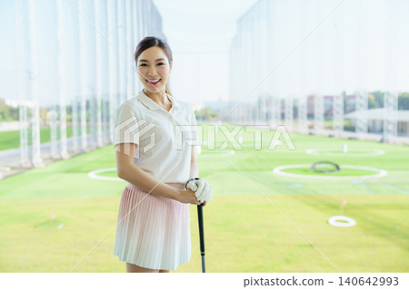 Woman golfer standing confidently at a driving range with golf club. 140642993
