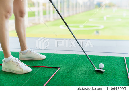 Close up of golfer preparing to hit golf ball on turf at driving range Close up of golfer preparing to hit golf ball on turf at driving range 140642995