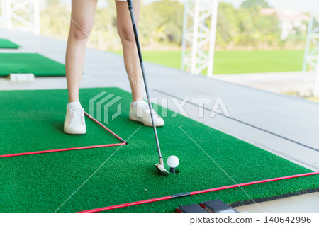 Close up of golfer preparing to hit golf ball on turf at driving range Close up of golfer preparing to hit golf ball on turf at driving range 140642996