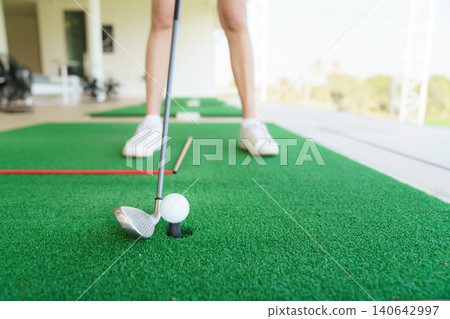 Close up of golfer preparing to hit golf ball on turf at driving range Close up of golfer preparing to hit golf ball on turf at driving range 140642997