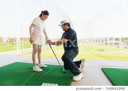 Golf coach giving hands-on instruction to beginner golfer at driving range. Golf coach giving hands-on instruction to beginner golfer at driving range. 140642998