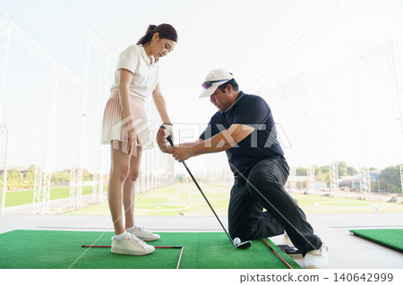 Golf coach giving hands-on instruction to beginner golfer at driving range. Golf coach giving hands-on instruction to beginner golfer at driving range. 140642999