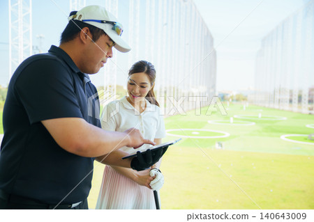 Golf instructor explaining swing technique on digital tablet to woman golfer at driving range. Golf instructor explaining swing technique on digital tablet to woman golfer at driving range. 140643009