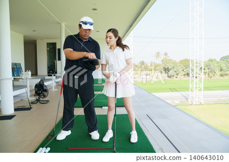 Golf instructor explaining swing technique on digital tablet to woman golfer at driving range. Golf instructor explaining swing technique on digital tablet to woman golfer at driving range. 140643010