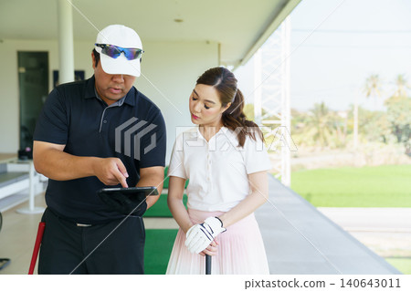 Golf instructor explaining swing technique on digital tablet to woman golfer at driving range. Golf instructor explaining swing technique on digital tablet to woman golfer at driving range. 140643011