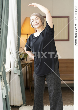 老婦人在客廳伸展身體 老婦人在客廳伸展身體 140643319